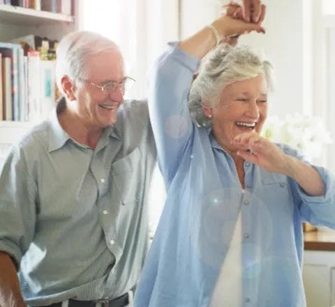 An elderly couple laughing and dancing together indoors