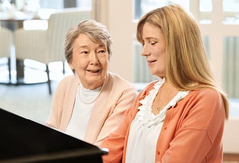Woman and senior sit by piano Senior watches as woman plays piano beside her.