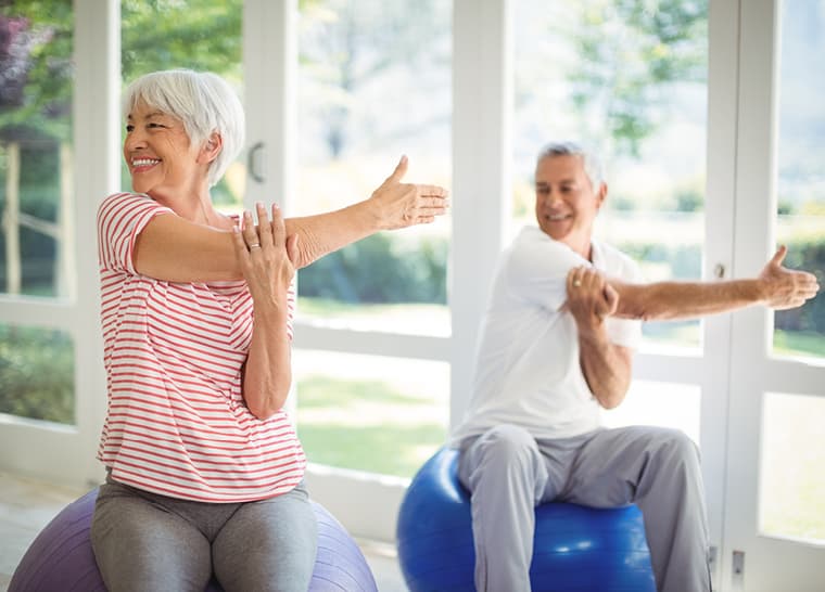 Pelvic and Bladder Health Exercise with Exercise Balls Senior woman and man smiling while stretching on exercise balls