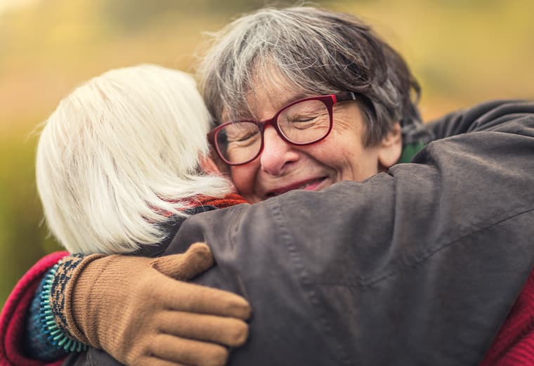 National Event photo - Grief and transition 1 Two seniors, dressed for winter, hug outside, smiling.