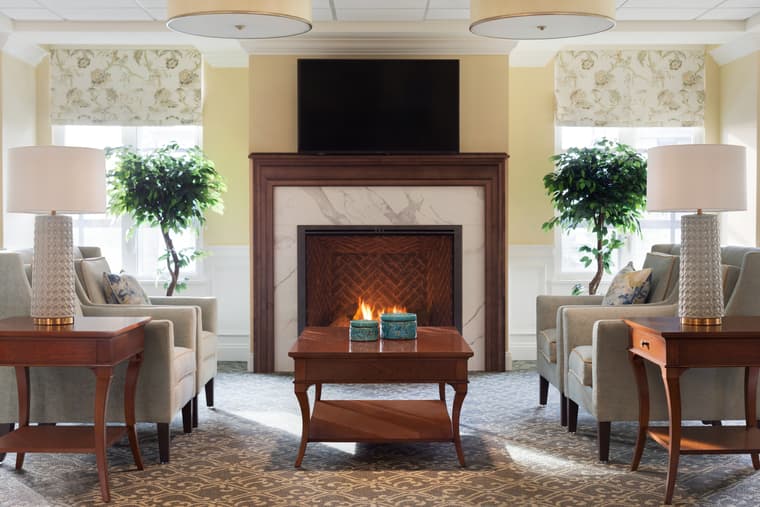 White Rock - Memory Care Lounge Memory care lounge with gray-beige armchairs, coffee table and a fireplace.